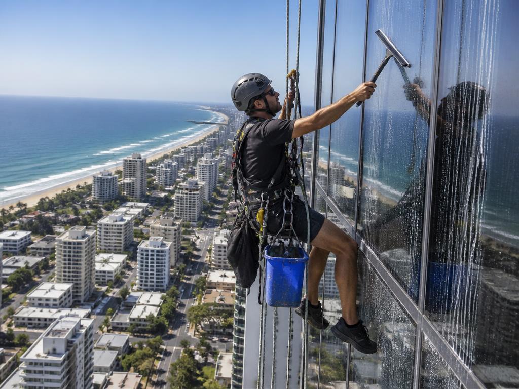 Trabajador con arnés limpiando vidrios de edificio en altura frente al mar